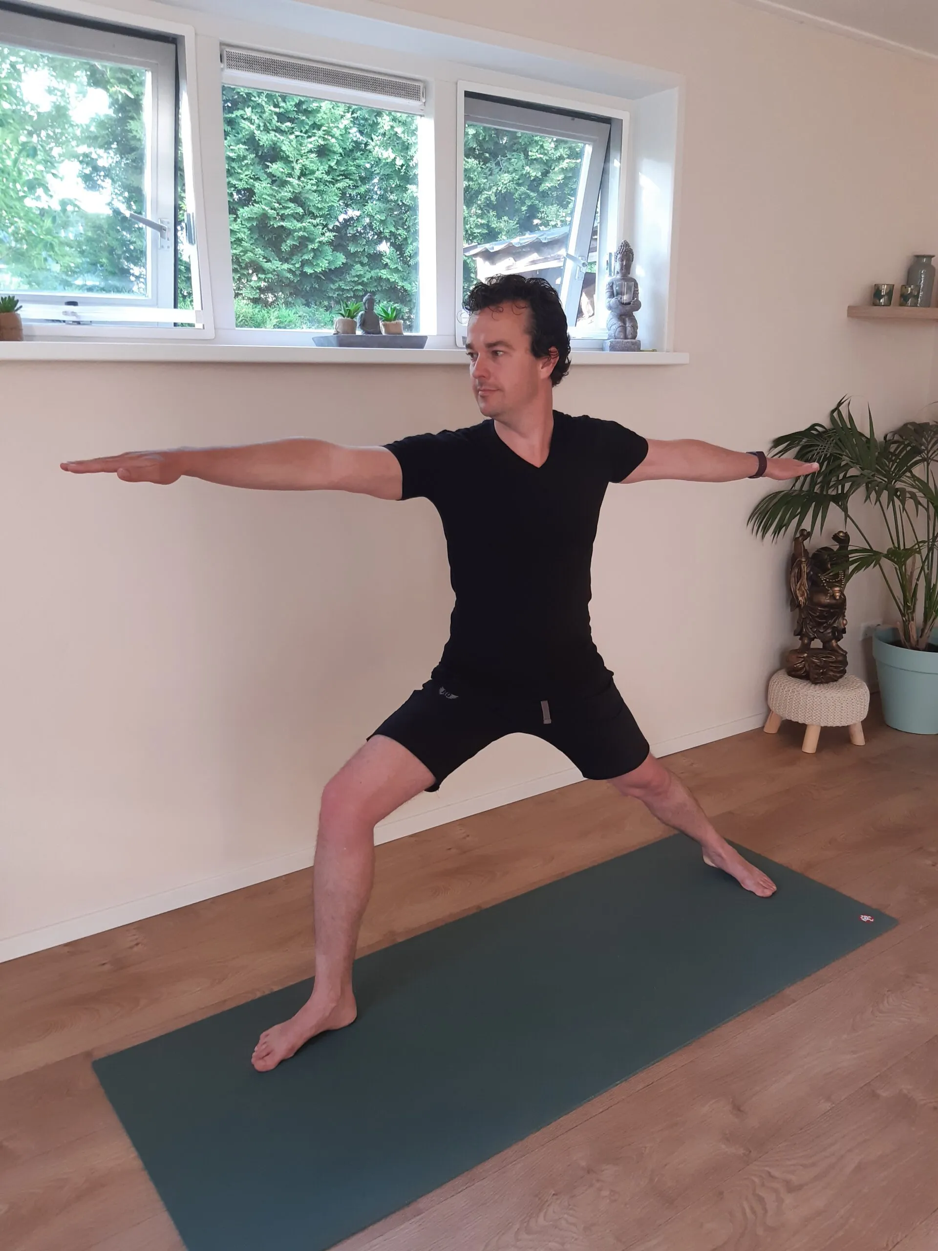 Een man in de houding van de krijger op een mat in de lichte yogaruimte