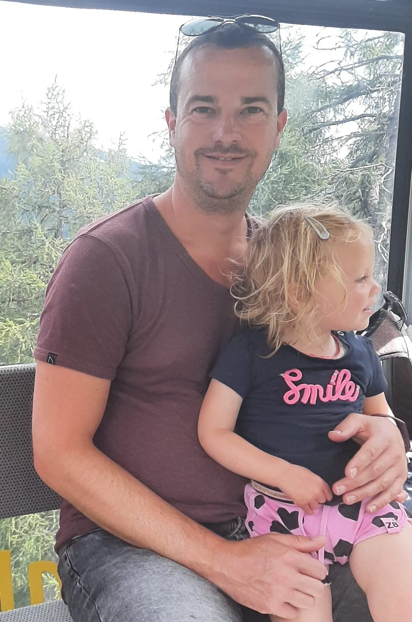 Roland met een kind op schoot, met bomen achter het raam